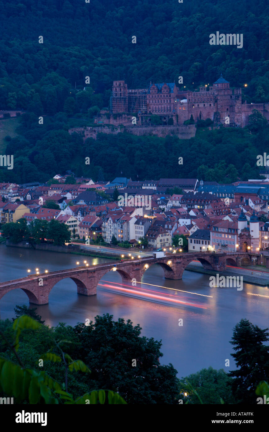 Les lumières d'une croisière en bateau la rivière sous un pont sur le Neckar sont floues, avec la ville de Heidelberg en arrière-plan. Banque D'Images