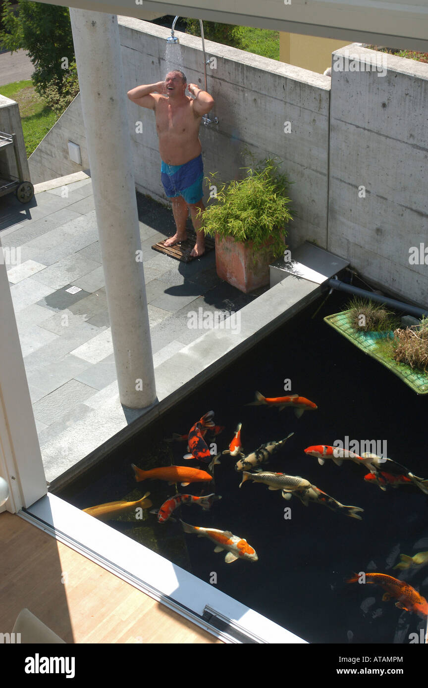 L'homme en prenant une douche près de la piscine un transformés en un étang du poisson pour carpes koï, Lupsingen, Suisse Banque D'Images