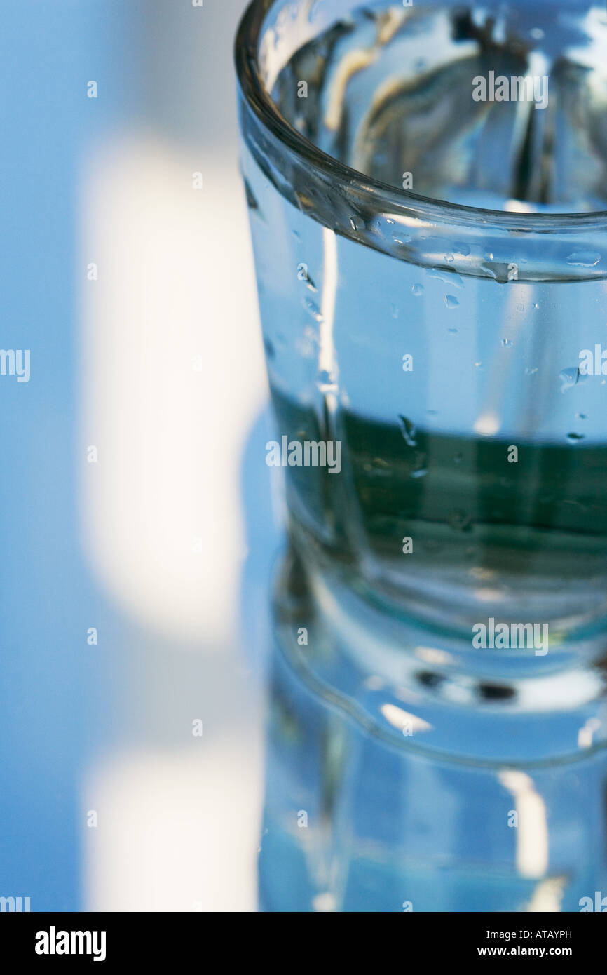 L'eau dans un verre qui se dresse sur un miroir qui reflète le ciel bleu Banque D'Images
