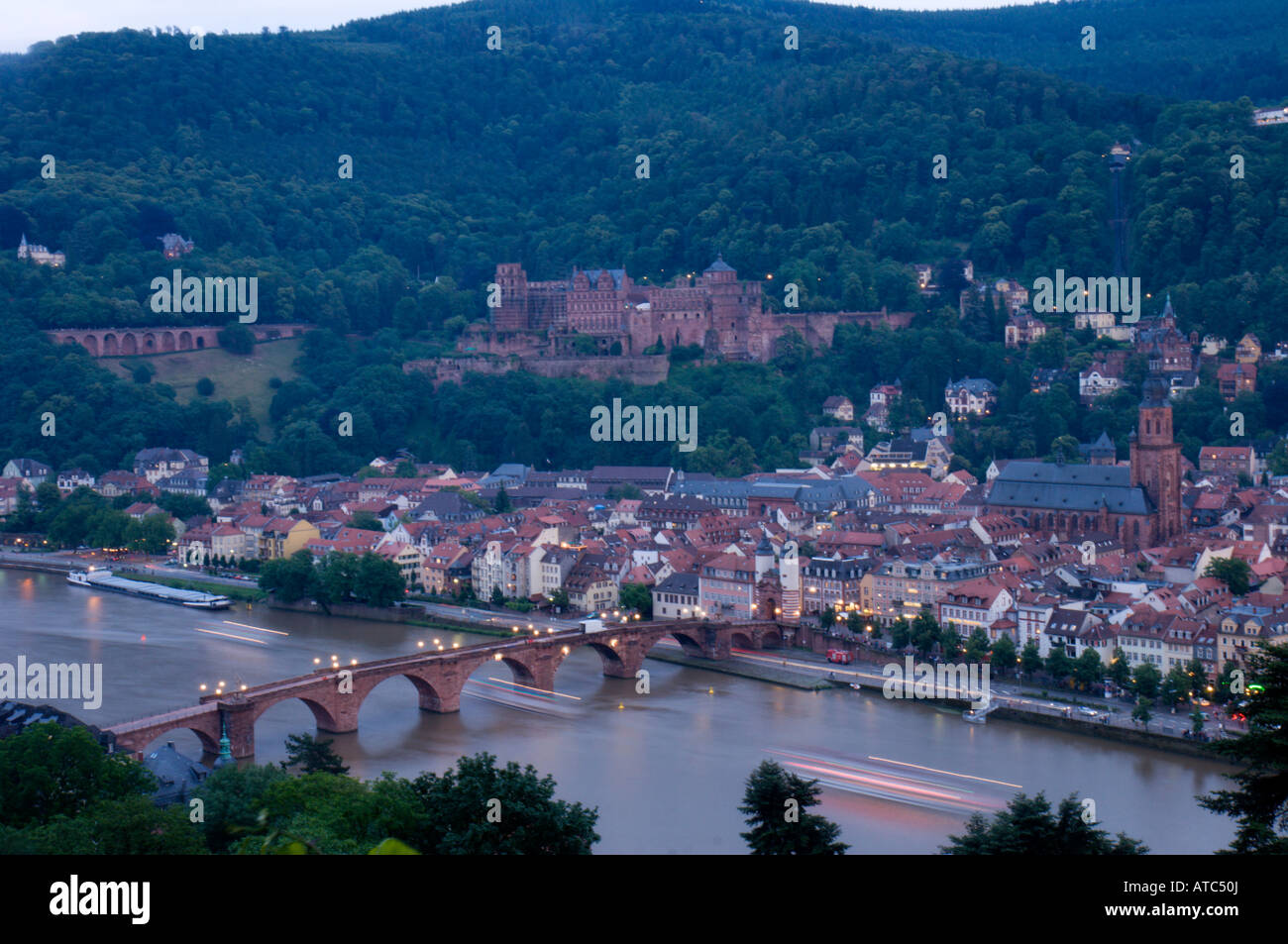 Les lumières d'une croisière en bateau la rivière sous un pont sur le Neckar sont floues, avec la ville de Heidelberg en arrière-plan. Banque D'Images