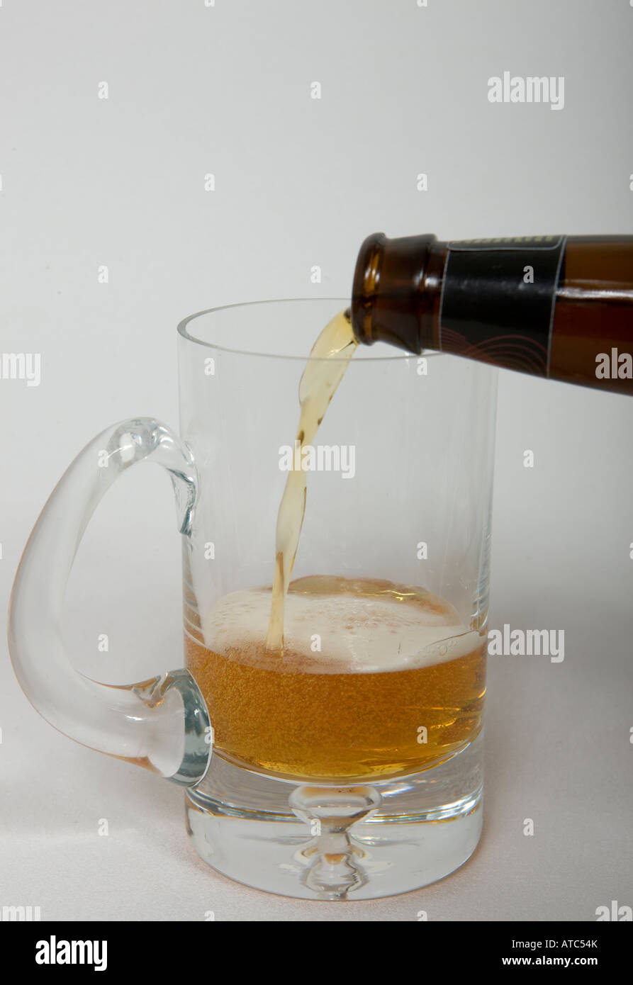 Beer mug avec bière ambrée est versé à partir d'une bouteille sur transparent blanc Banque D'Images