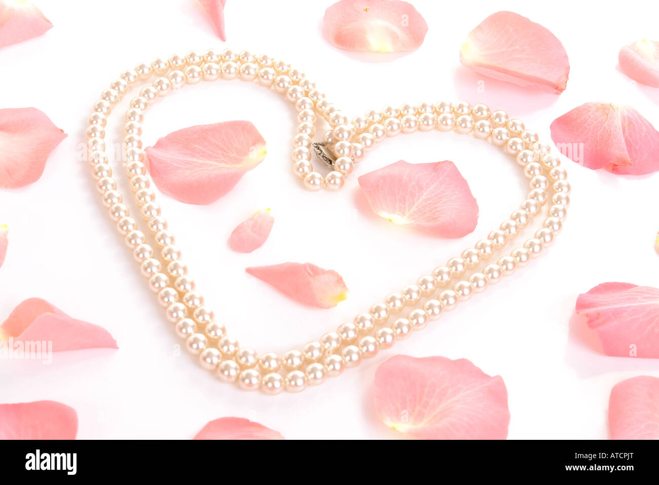 Forme de coeur créé par chaîne de perles parmi les pétales de roses éparpillées sur un fond blanc Banque D'Images