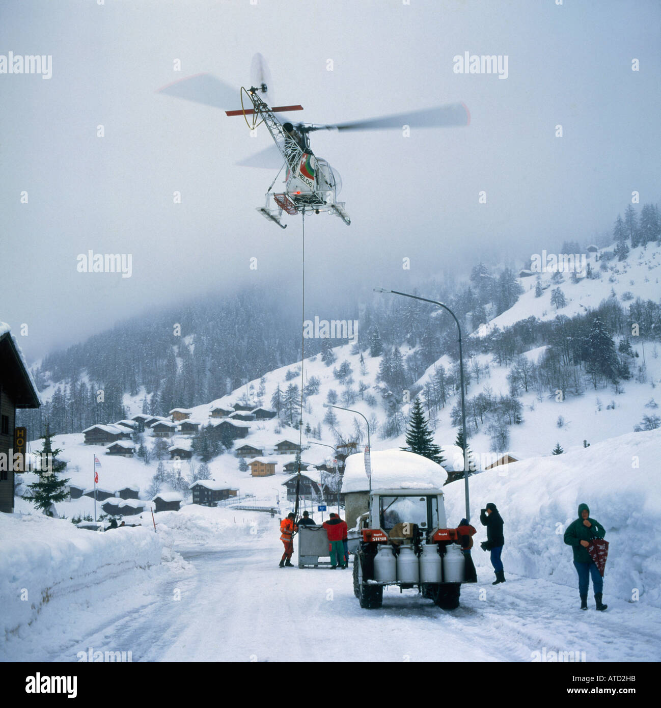 La collecte de fournitures d'urgence par hélicoptère à partir de lait tracteur ci-dessous sur la route couverte de neige en Valais Suisse village Ritzingen Banque D'Images