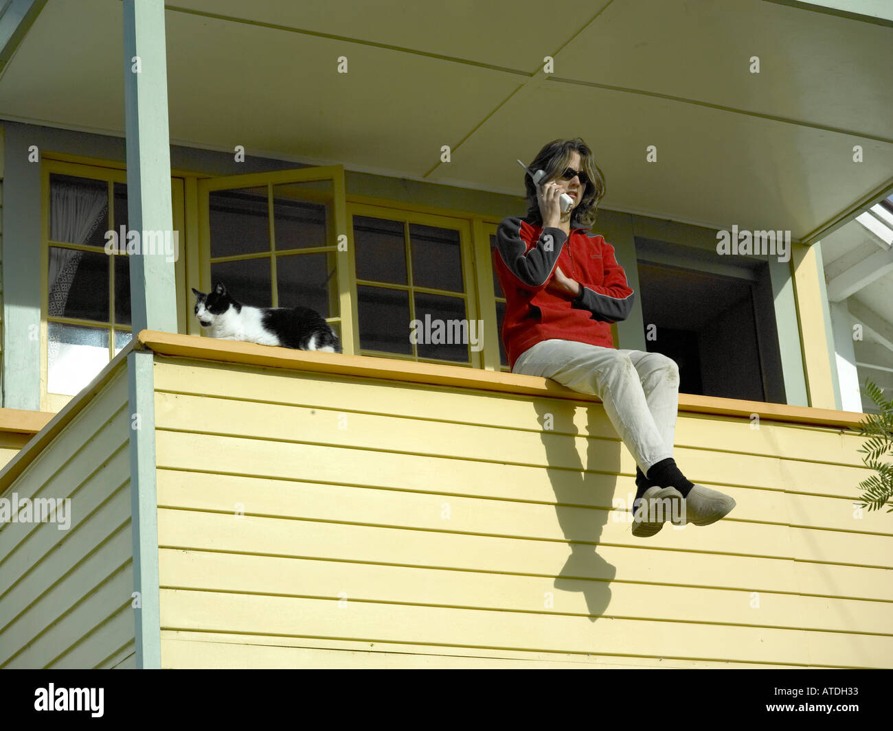 Femme assise sur le balcon à parler au téléphone avec chat noir et blanc sur une chaude journée d'été ensoleillée et Banque D'Images