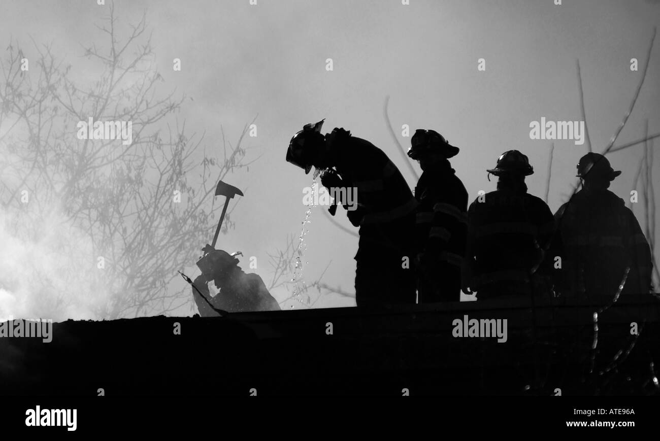 Les pompiers sur un toit, l'eau potable dans leur lutte contre l'incendie Banque D'Images