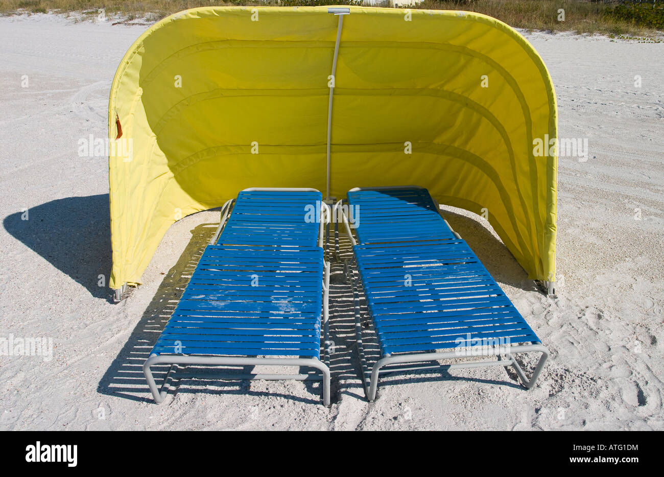 L'abri du vent en jaune. Deux chaises longues de plage bleu en dessous d'une toile jaune soleil et vent sur une plage de sable blanc Banque D'Images