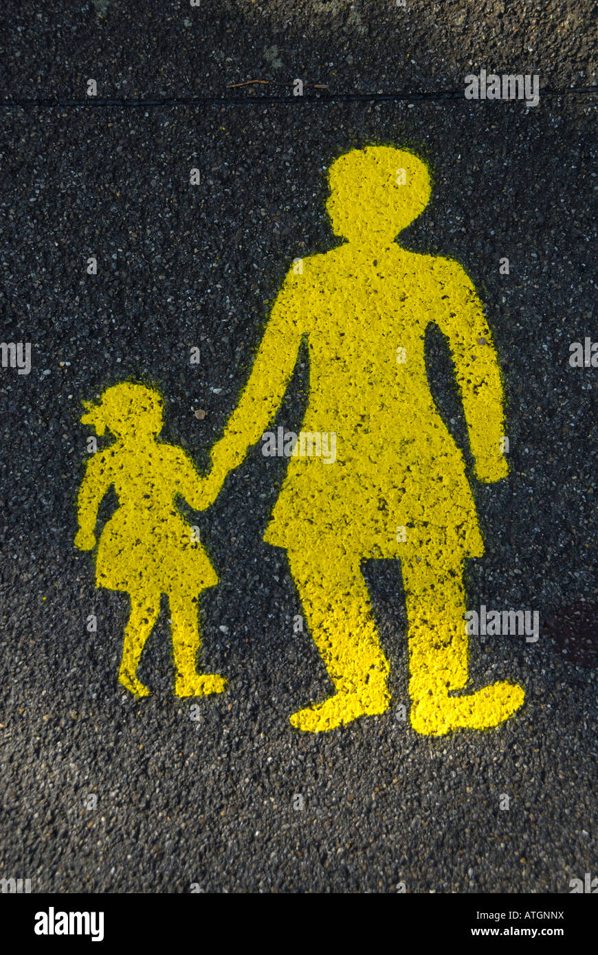 Un panneau jaune peint sur une route mouillée d'un enfant tenant la main de sa mère. Banque D'Images