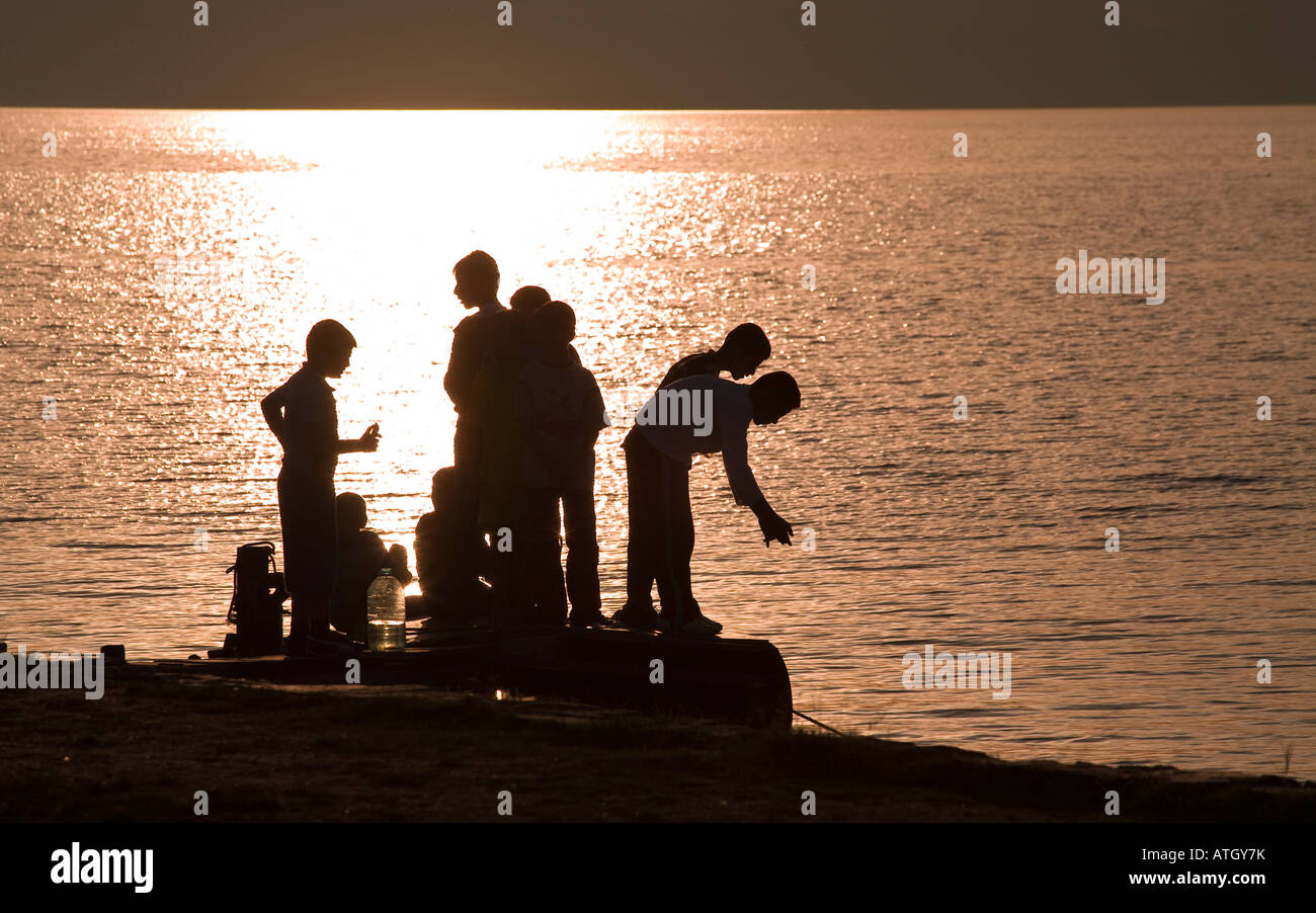 Pêche à la ligne à partir de la station d'un groupe de garçons en silhouette chats et des poissons d'un petit quai sur le côté du lac Banque D'Images