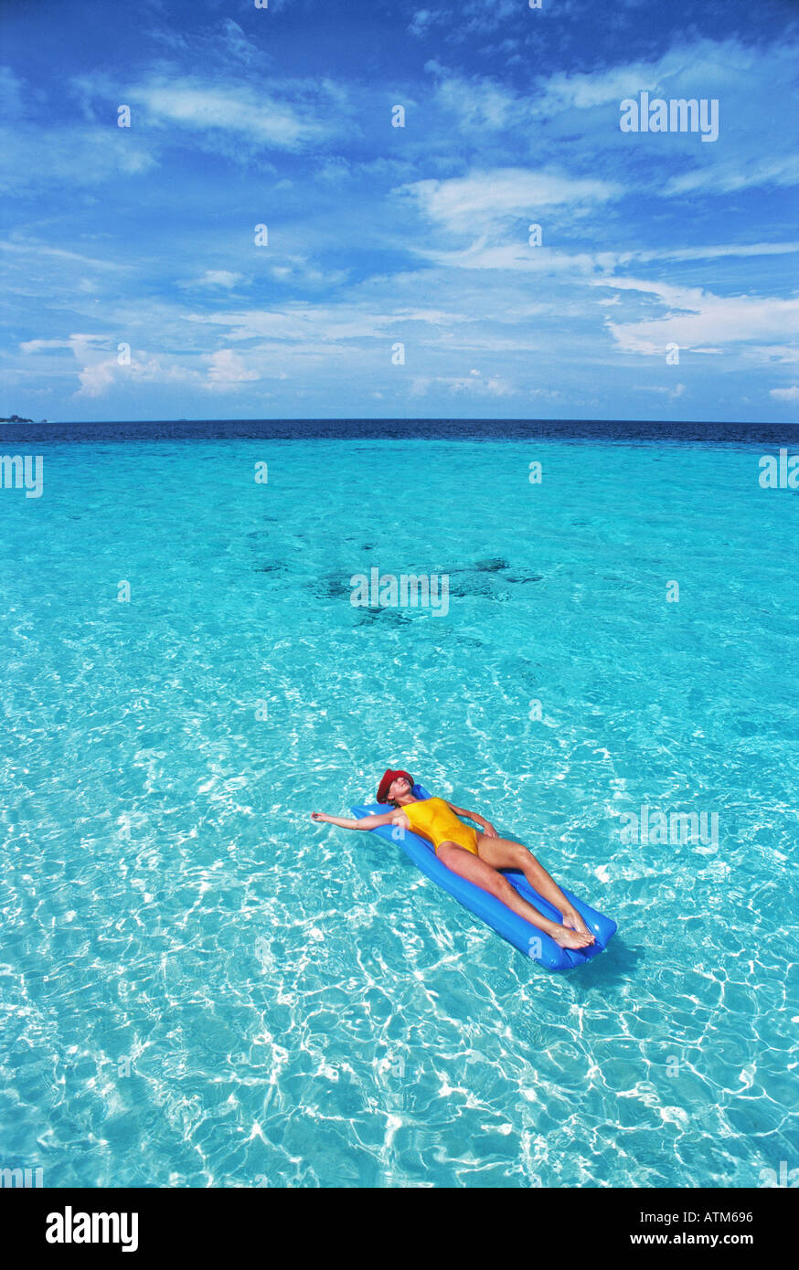 Woman relaxing in paradise sur matelas d'air entre les eaux claires aqua bleu et blanc des nuages filandreux Banque D'Images