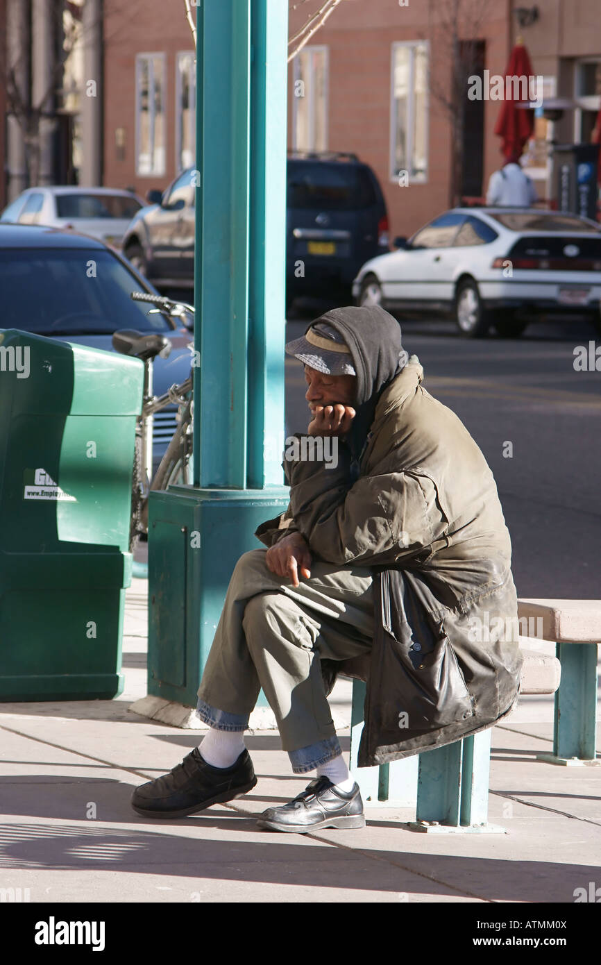 Un sans-abri triste homme assis sur un banc public dans une zone du centre-ville. Banque D'Images