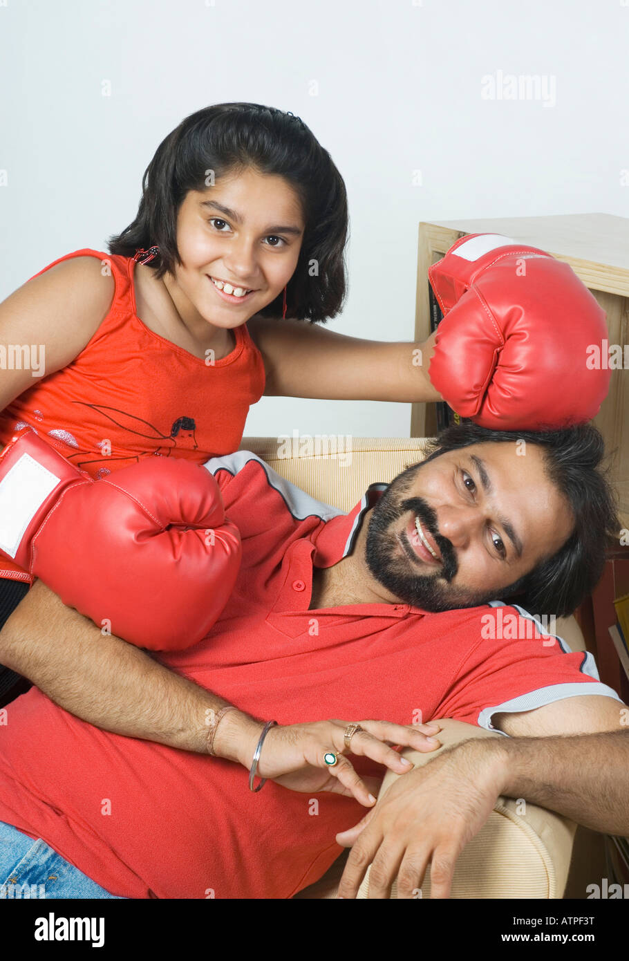 Portrait of a Mid adult man reclining on a couch avec sa fille wearing boxing gloves Banque D'Images