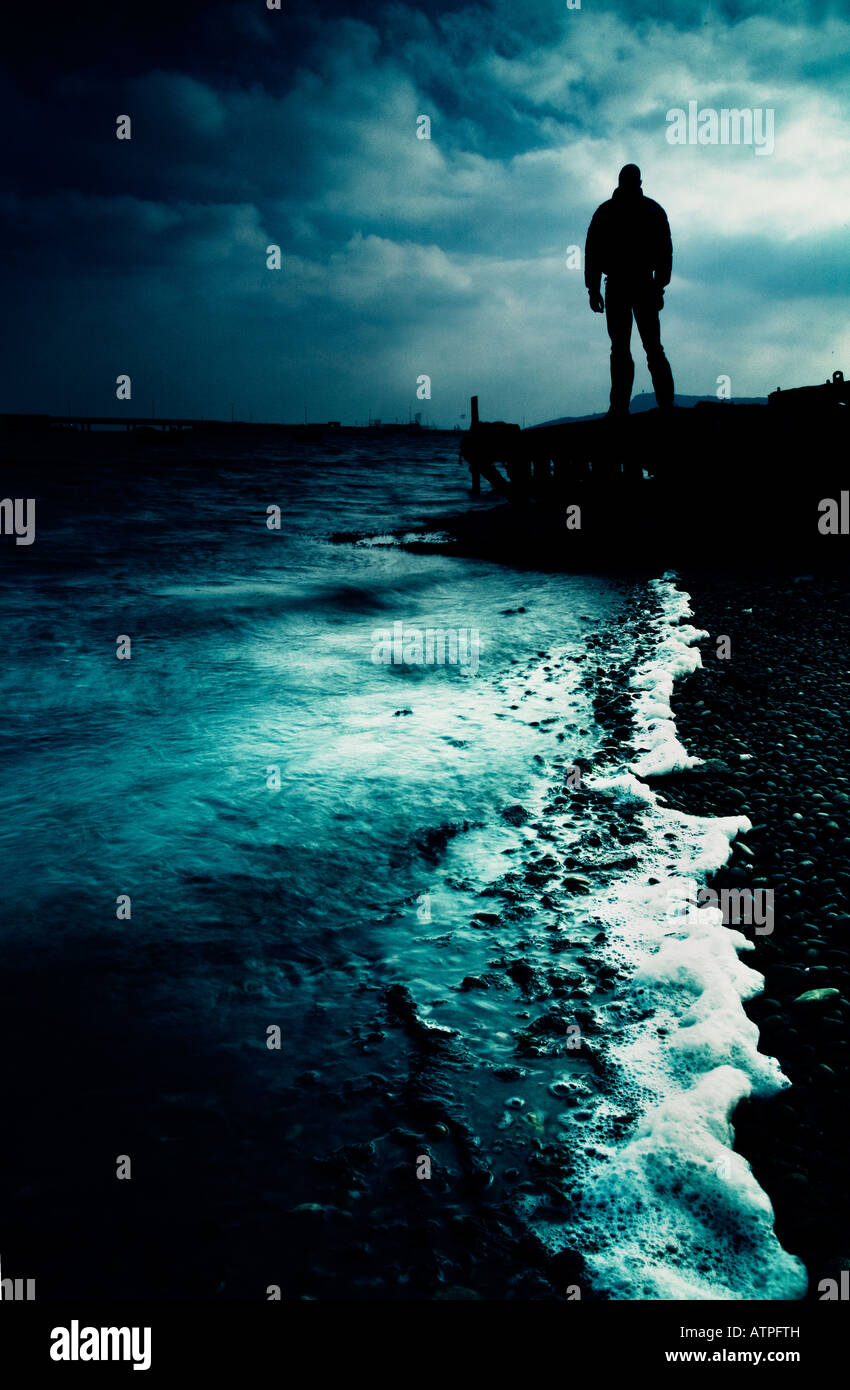 La figure sombre standing on jetty looking out to sea Banque D'Images