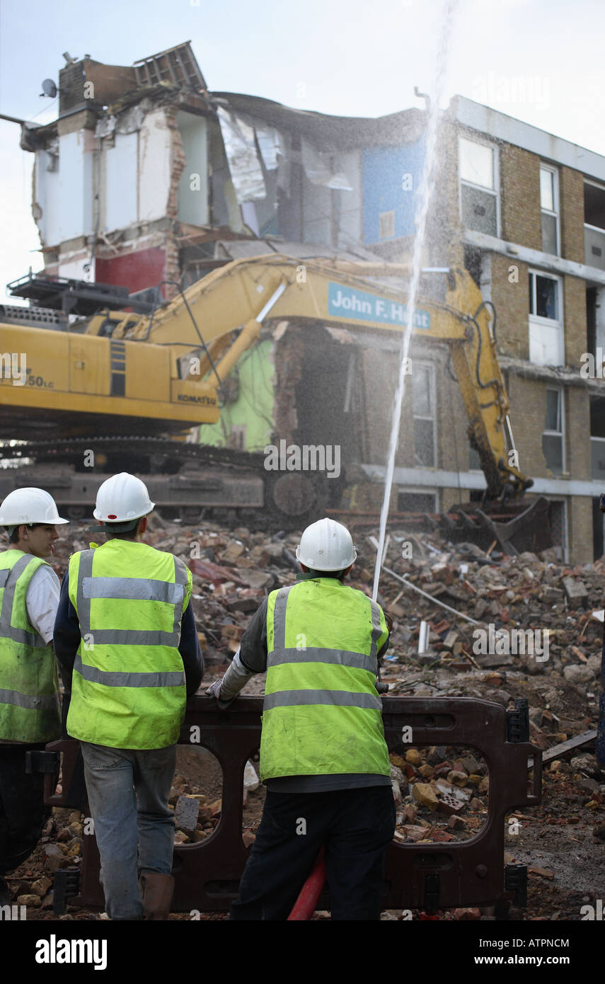 Les travailleurs de la construction modérer la poussière avec un flexible d'eau au cours de la démolition d'un ensemble immobilier. Banque D'Images