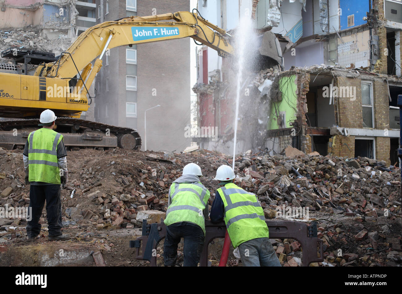Les travailleurs de la construction modérer la poussière avec un flexible d'eau au cours de la démolition d'un ensemble immobilier. Banque D'Images