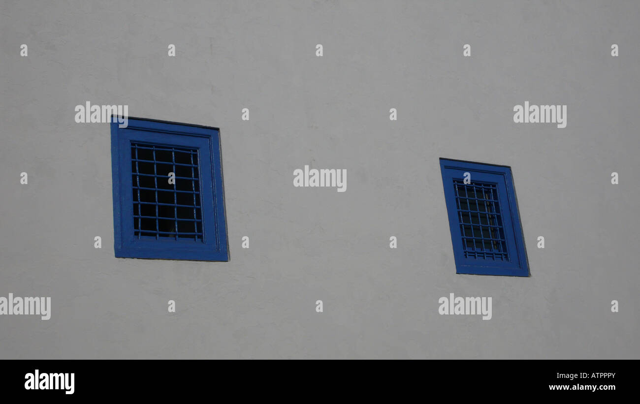 Extérieur d'un bâtiment traditionnel avec de petites fenêtres bleues et des murs blanchis à la chaux à Sidi Bou Said, une ville balnéaire près de Tunis, en Tunisie. Banque D'Images