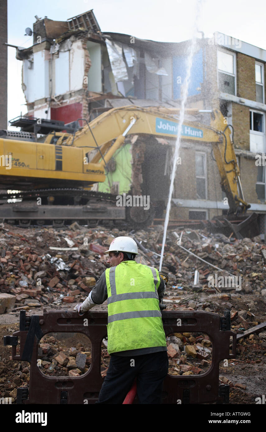 Un travailleur de la construction ralentit vers le bas la poussière avec un flexible d'eau au cours de la démolition d'un ensemble immobilier. Banque D'Images