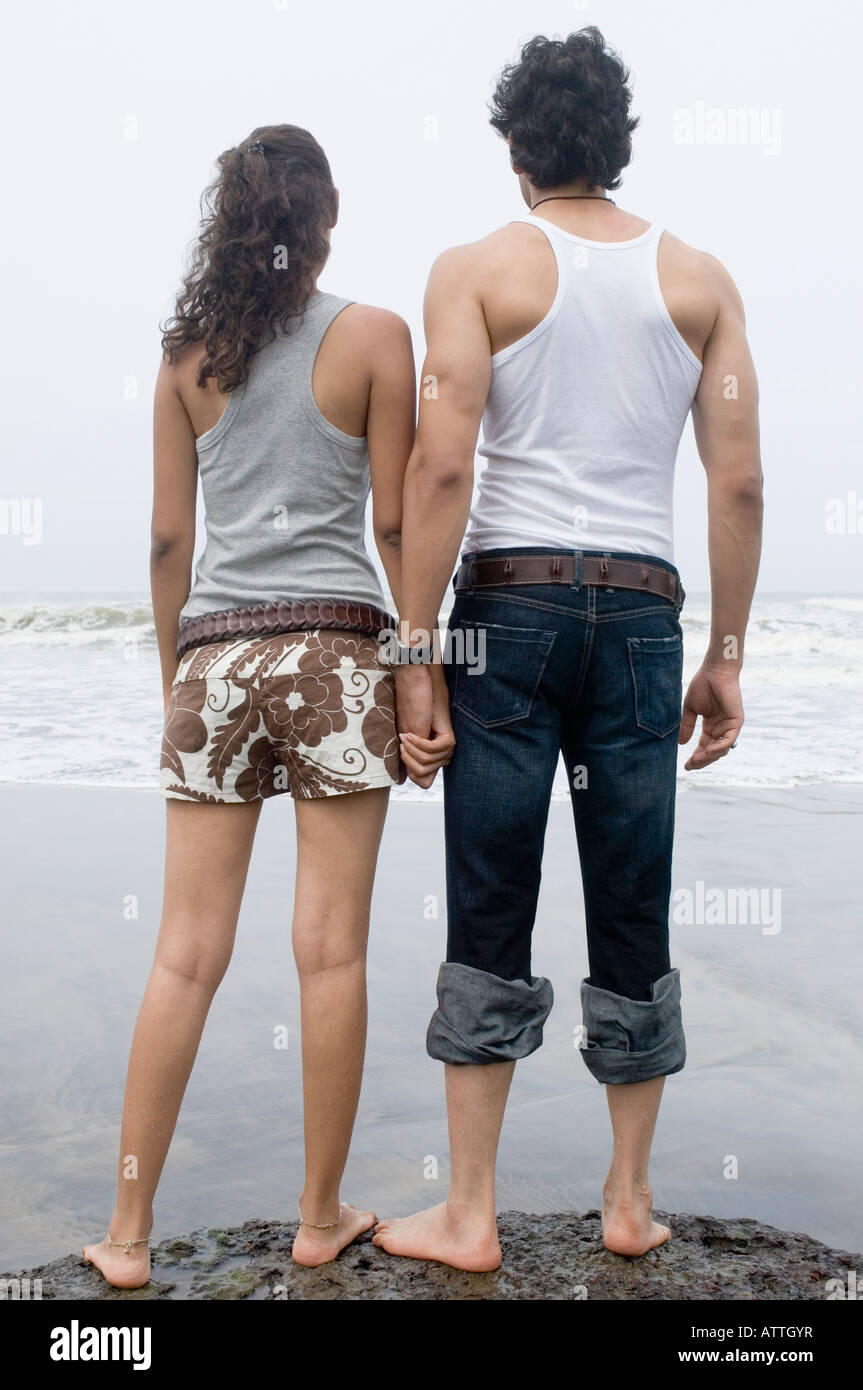 Vue Arriere D Un Jeune Couple Qui Se Tiennent La Main Debout Sur La Plage Photo Stock Alamy