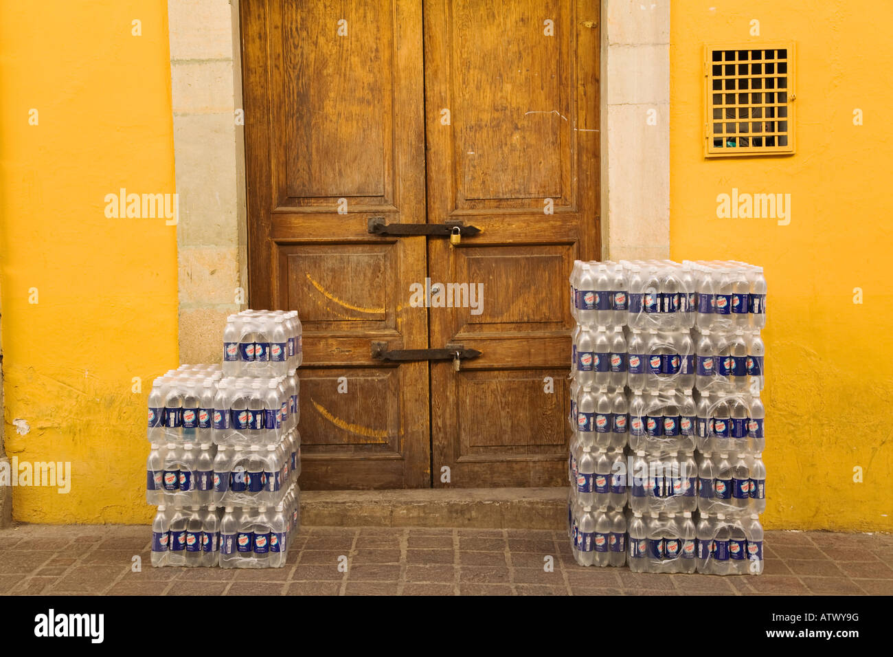 Mexique Guanajuato Les cas de l'eau en bouteille enveloppée dans du plastique sur trottoir cadenassé la porte en bois Banque D'Images