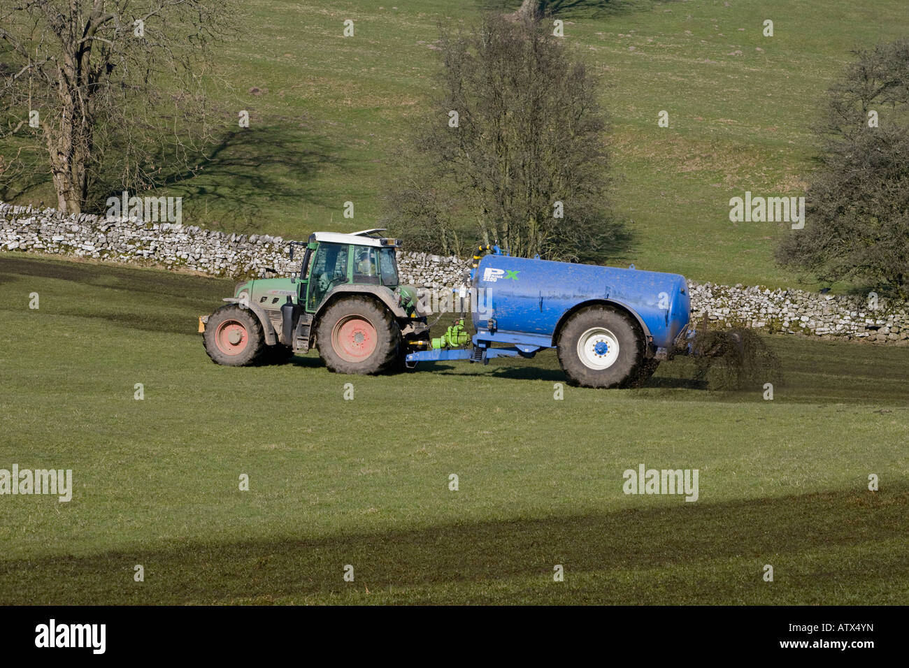 Agriculteur travaillant à la conduite d'un tracteur vert et d'un réservoir d'engrais cylindrique pulvérisant du lisier sur des pâturages agricoles - Yorkshire, Angleterre, Royaume-Uni Banque D'Images