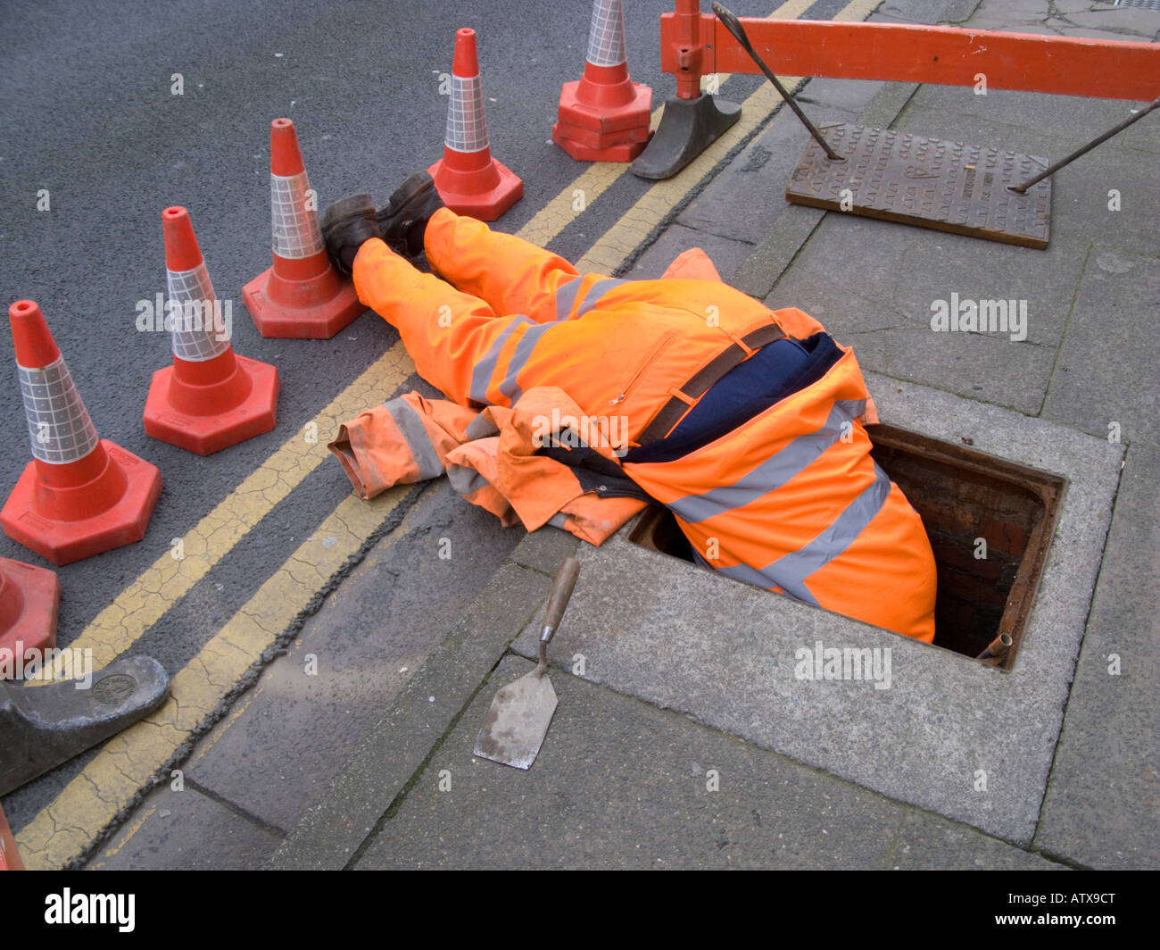 Dyno Rod worker wearing salopette orange tête première dans un égout à la recherche d'une obstruction dans les tuyaux Banque D'Images