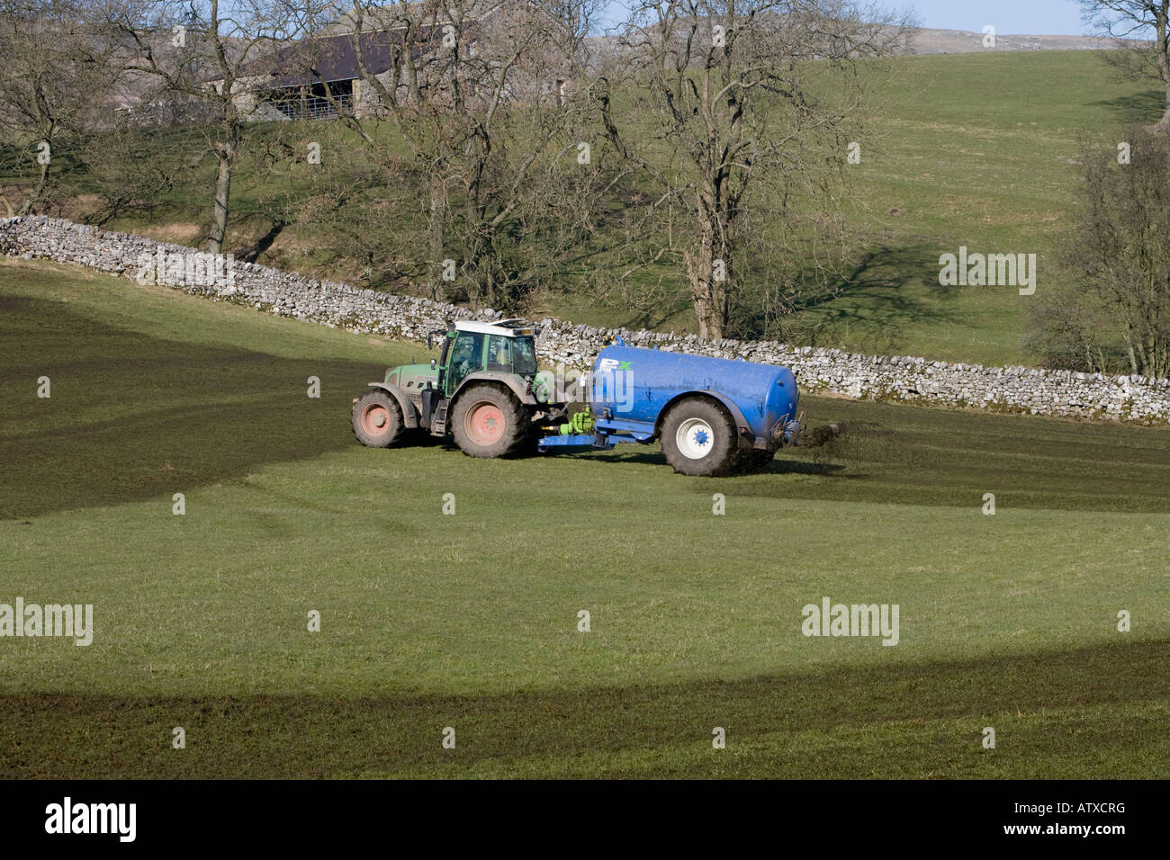 Agriculteur travaillant à la conduite d'un tracteur vert et d'un réservoir d'engrais cylindrique pulvérisant du lisier sur des pâturages agricoles - Yorkshire, Angleterre, Royaume-Uni Banque D'Images