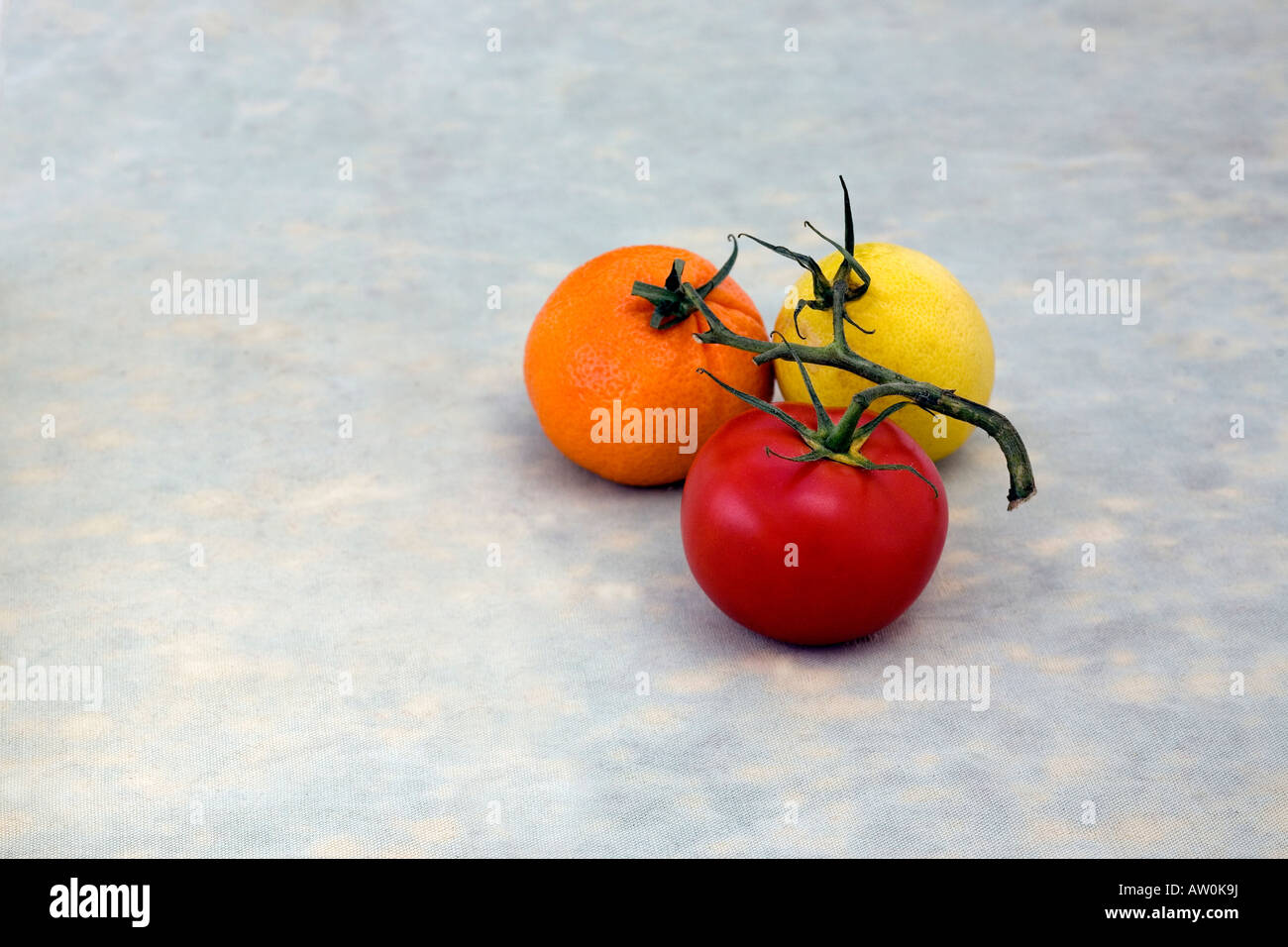 Une tomate rouge, jaune citron et une orange fruits manderin sont connectés sur une vigne. Ils sont sur un fond gris vert bleu Banque D'Images