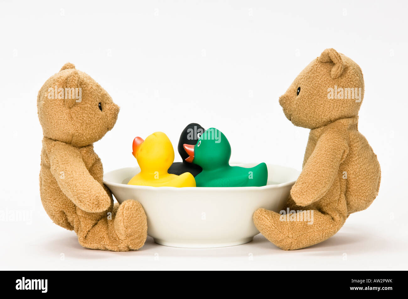 Deux ours brun en peluche regarder trois canards colorés dans une coupe bol blanc Banque D'Images