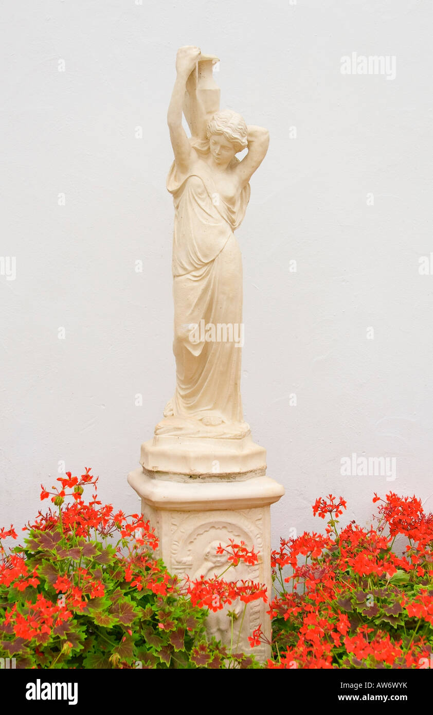 Statue de jardin décorative en forme de déesse et entouré de Pélargonium rouge dans le jardin de style italien Banque D'Images