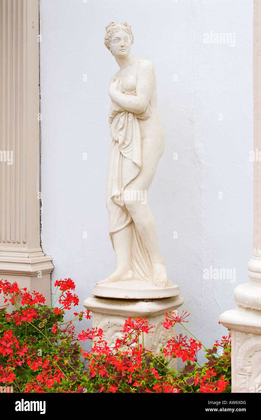 Statue de jardin décorative en forme de déesse et entouré de Pélargonium rouge dans le jardin de style italien Banque D'Images