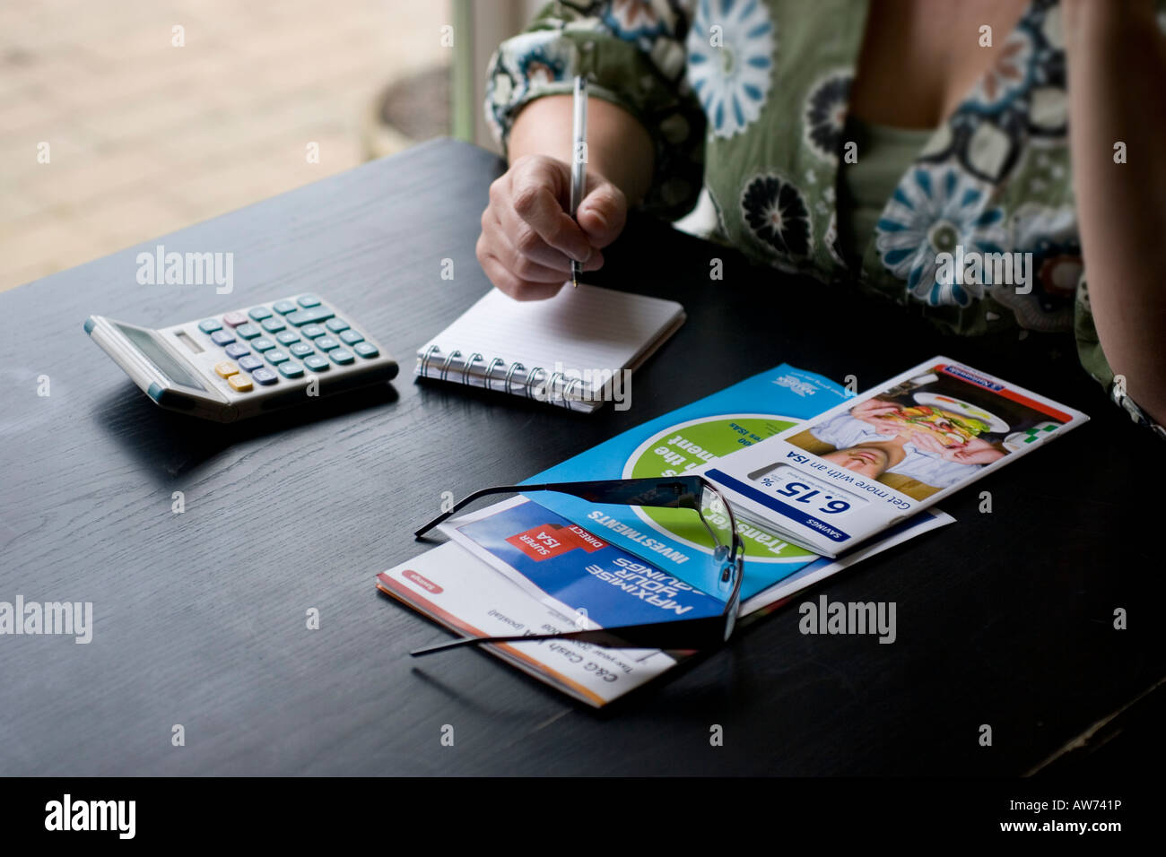 Femme étudiant et prenant des notes sur les brochures de compte d'épargne individuel ISA sur table avec calculatrice et bloc-notes Banque D'Images