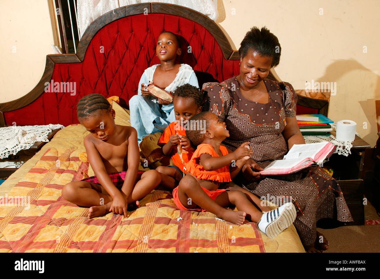 Mère avec des enfants sur un lit de la lecture à haute voix, Gaborone, Botswana, Africa Banque D'Images