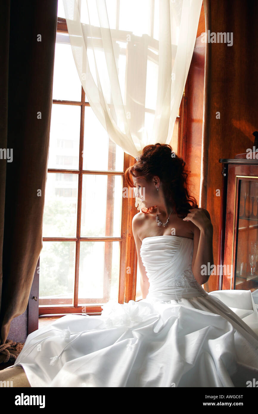Mariée assise par des rideaux dans la chambre Banque D'Images
