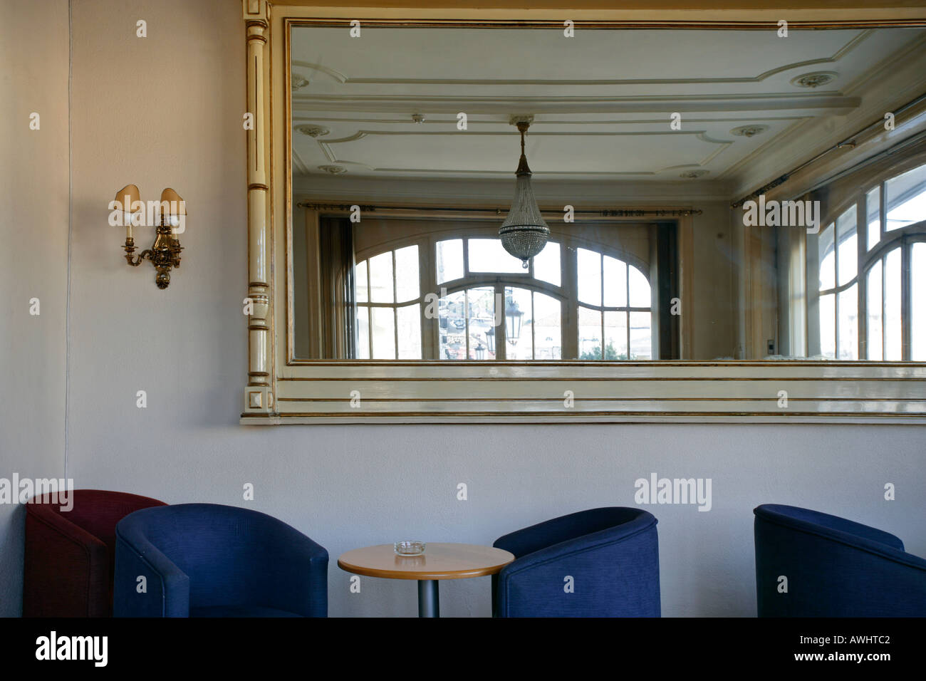 Une salle vide avec un grand miroir doré chaise rembourrée d'un lustre et de fenêtres ensoleillées Banque D'Images
