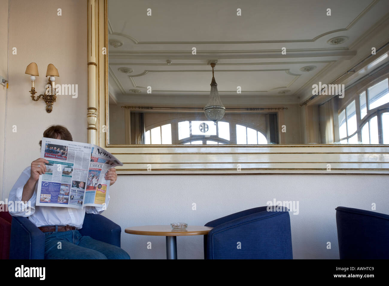 Un homme lit le journal dans une salle vide avec un grand miroir doré. Banque D'Images