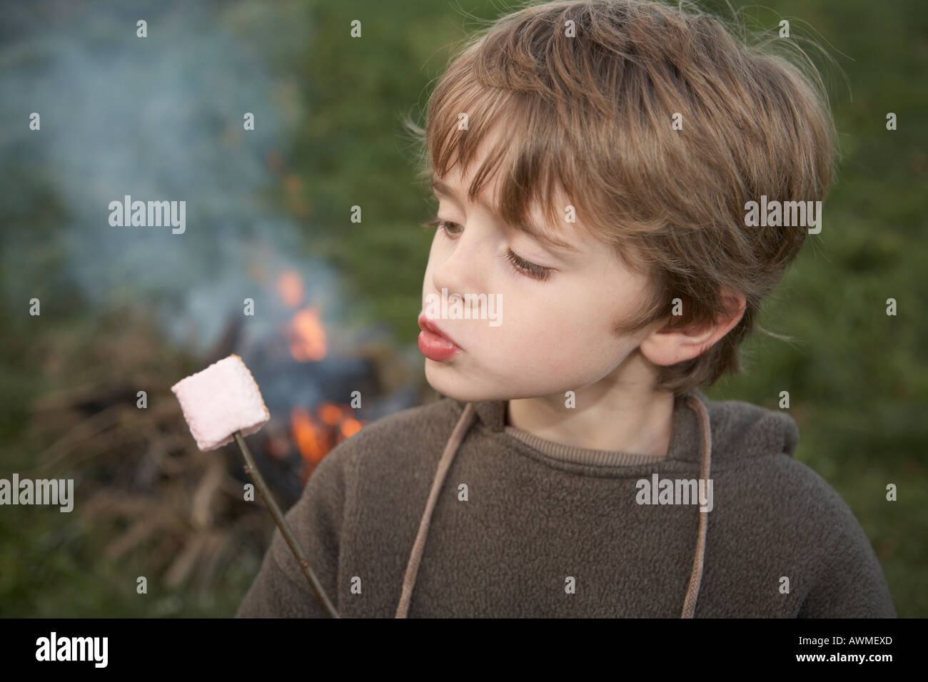Enfant toasting marshmallows dans jardin à l'extérieur et en soufflant dessus pour la refroidir Banque D'Images