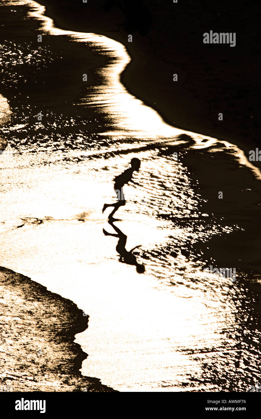 Silhouette de garçon s'exécutant sur une plage Banque D'Images