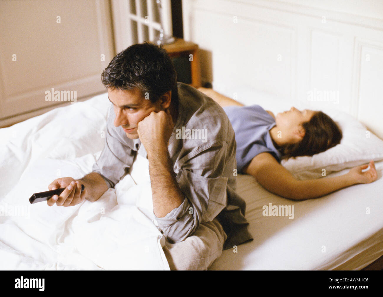 Homme assis dans son lit, en pointant la télécommande, femme couchée derrière lui. Banque D'Images