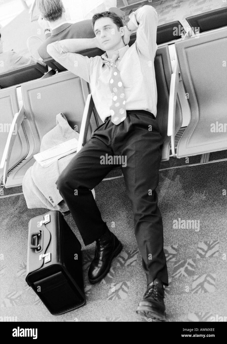 Businessman in airport lounge se penchant en arrière dans le siège, noir et blanc. Banque D'Images