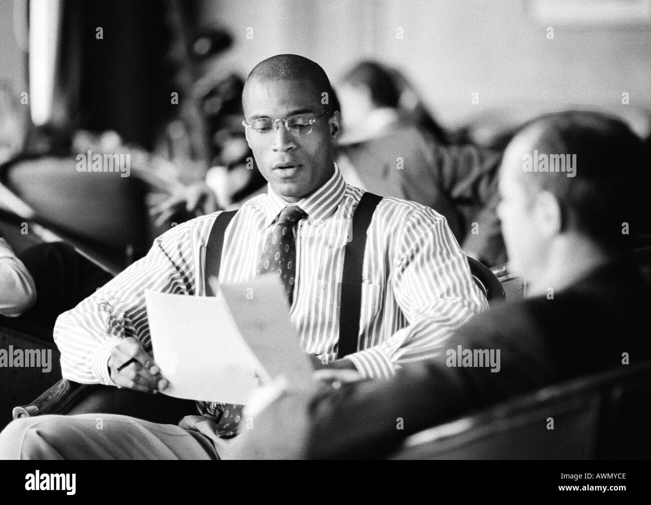 Les hommes d'affaires assis ensemble à la recherche de plus de documents, b&w. Banque D'Images