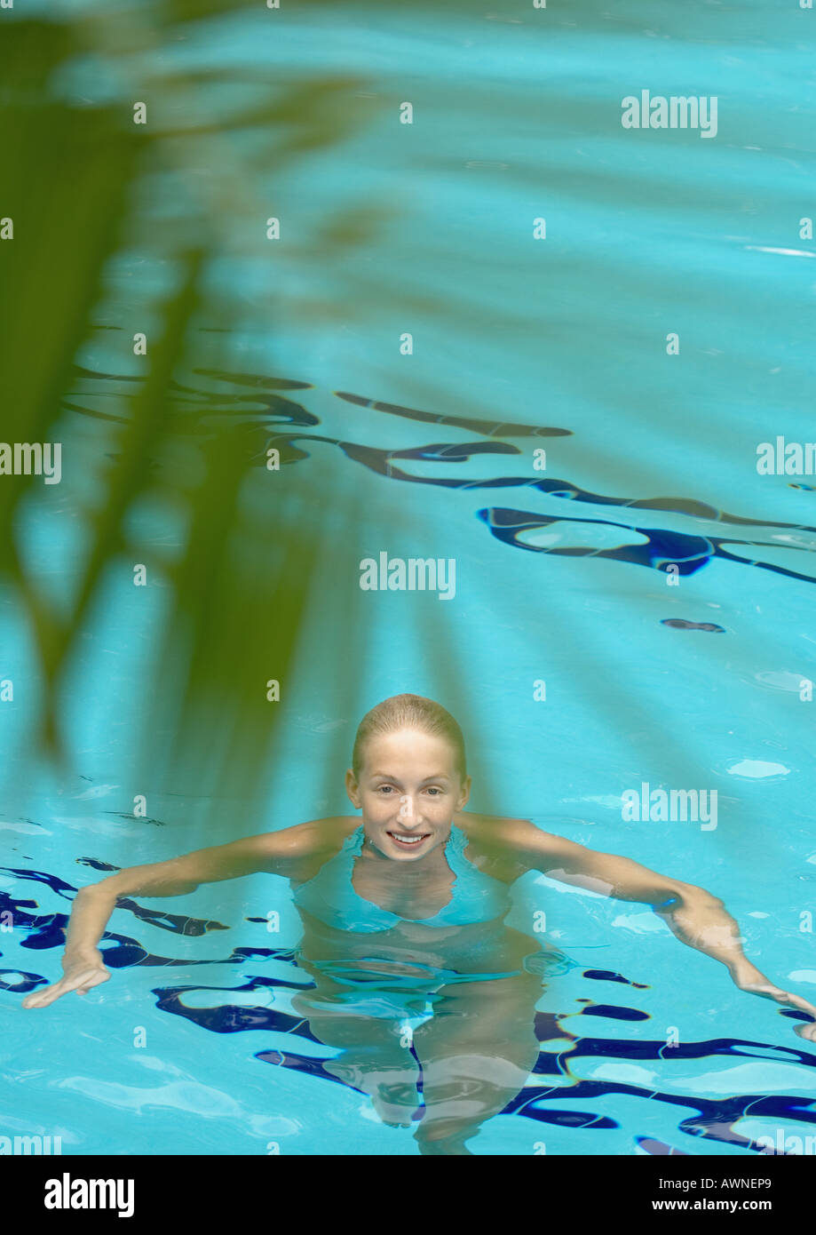 Femme debout dans la piscine, smiling at camera, la feuille de palmier en premier plan Banque D'Images