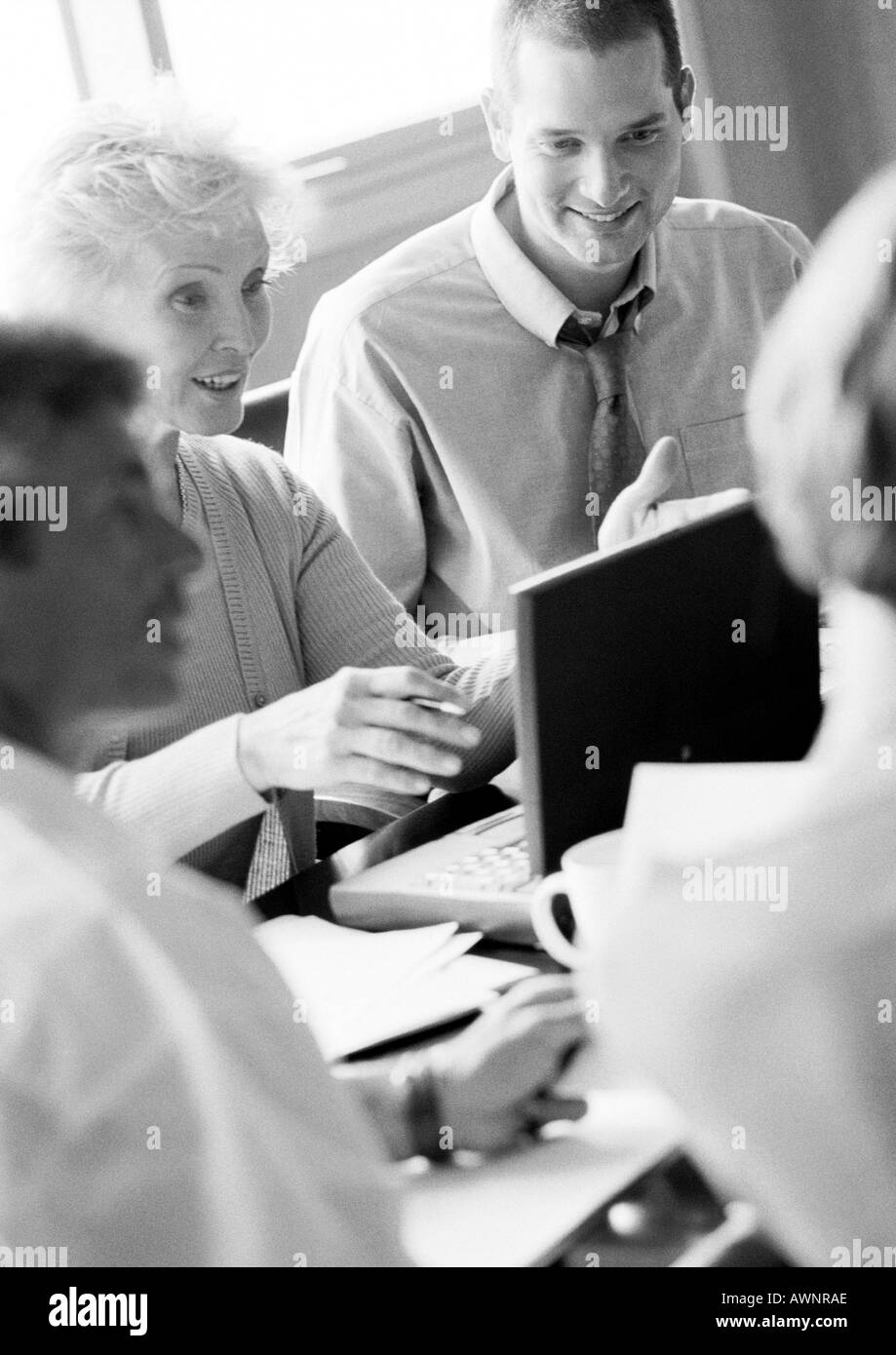 Young businesswoman in conference, à l'aide d'ordinateur portable, avec d'autres gens d'affaires, B&W Banque D'Images