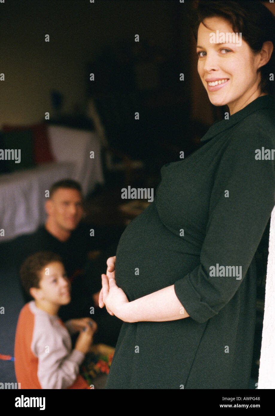 Femme enceinte debout et tenant de l'estomac, l'homme et enfant assis en arrière-plan Banque D'Images