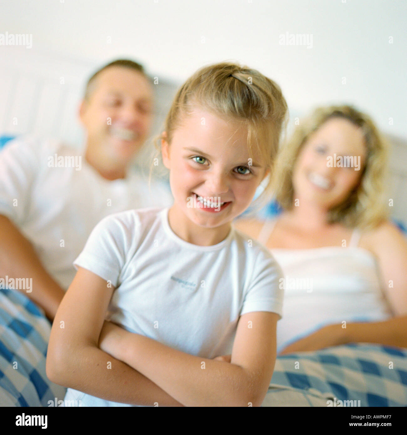 Girl folding arms and smiling in front of parents in bed, portrait Banque D'Images
