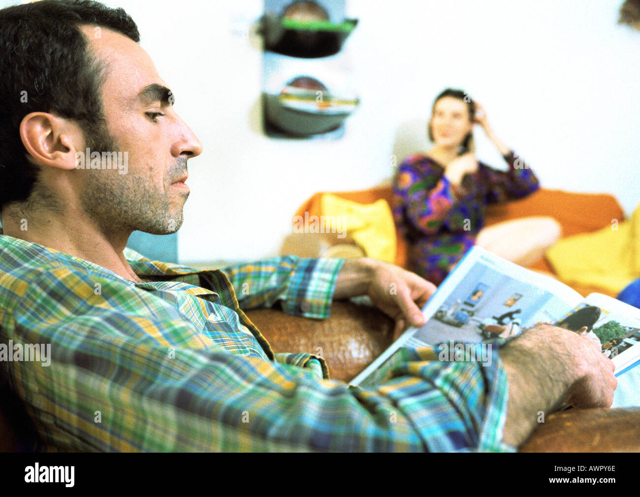 Man reading magazine, femme assise en arrière-plan. Banque D'Images