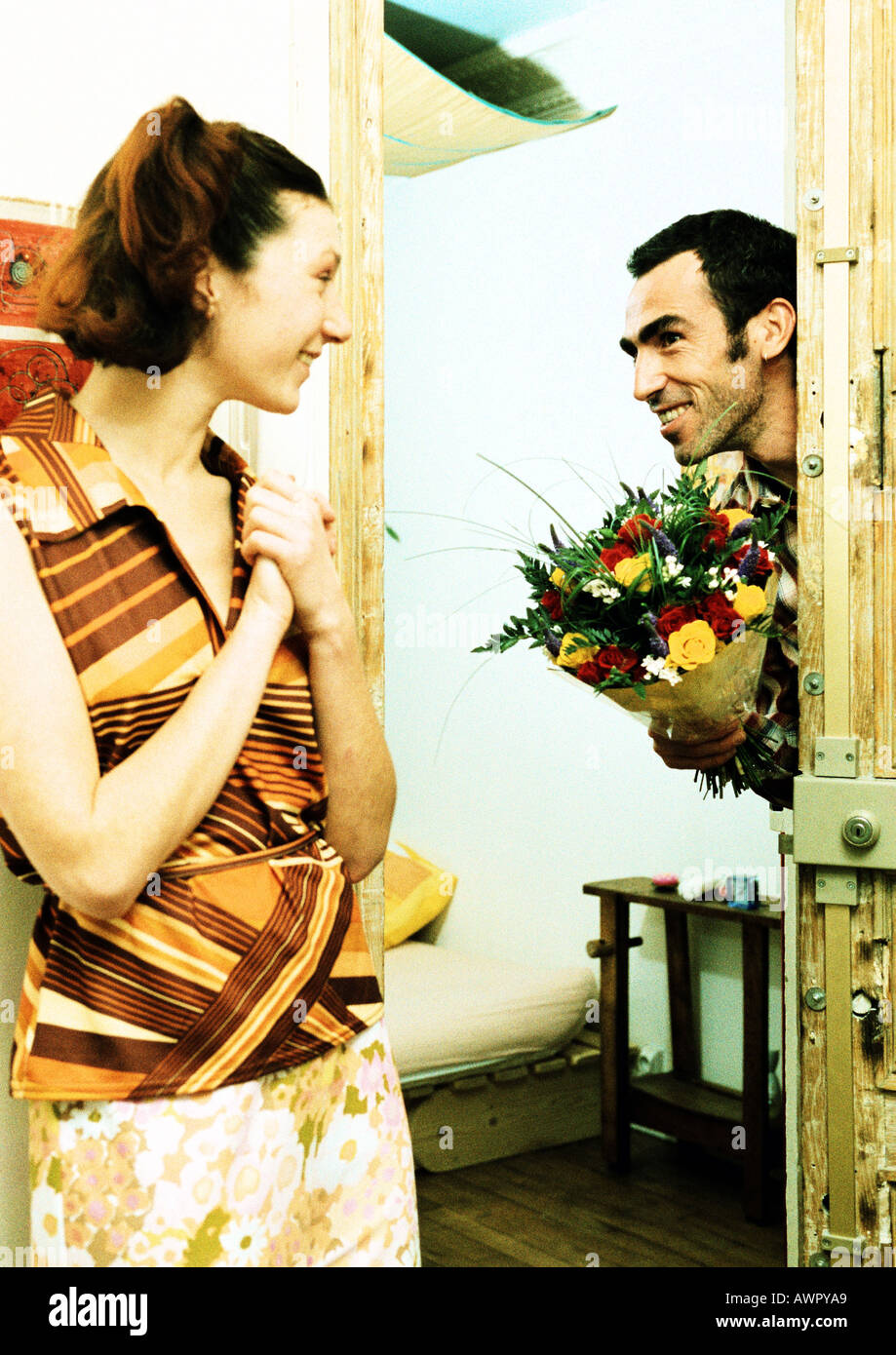 Couple, man walking through door holding bouquet de fleurs, woman smiling. Banque D'Images