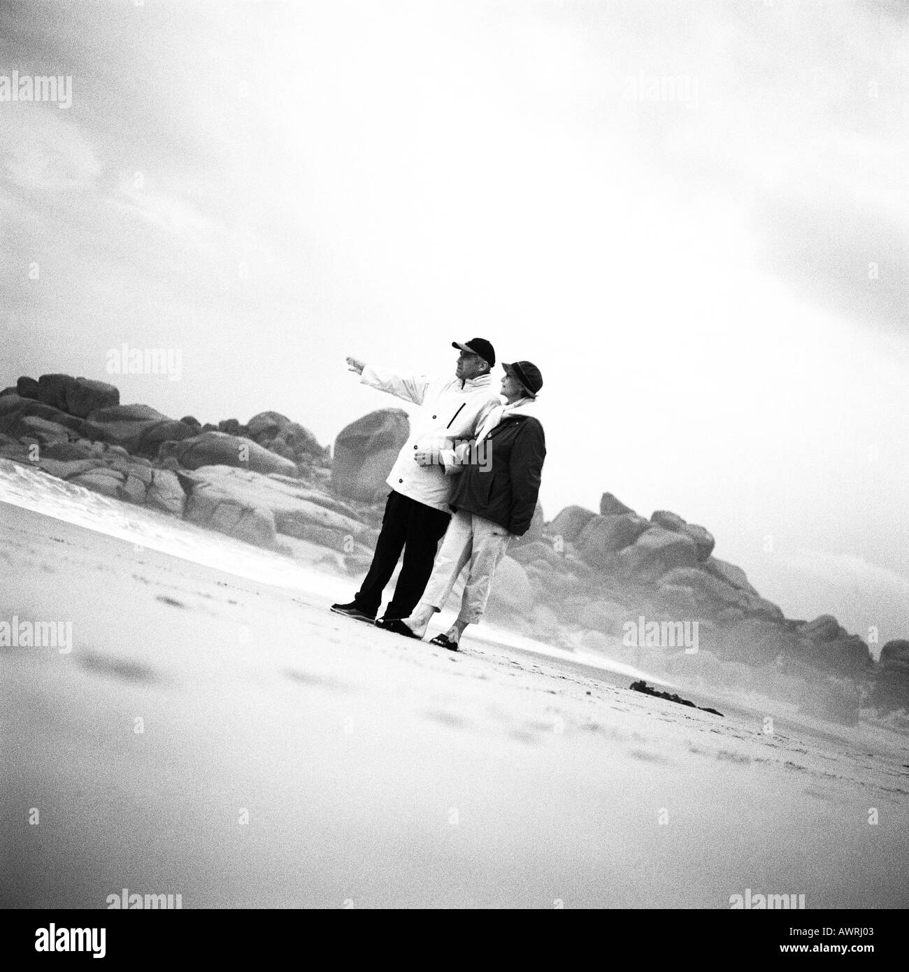 Mature couple standing on beach, man pointing, b&w Banque D'Images