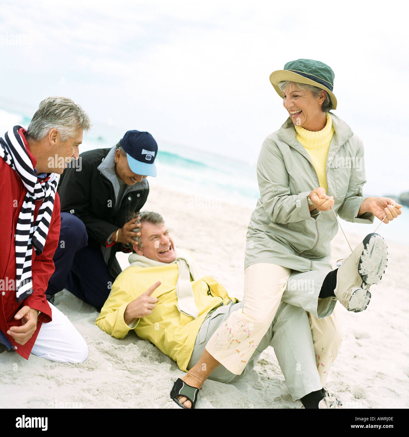 Groupe mature jouant sur plage, woman pulling man's laces Banque D'Images