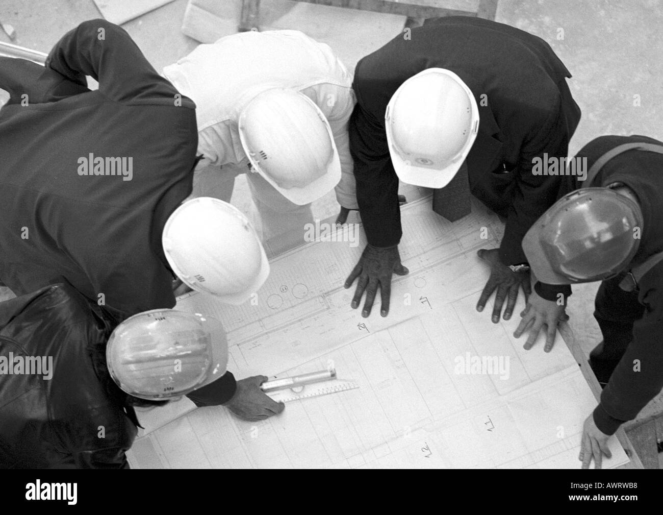 Cinq personnes avec des casques, examining blueprints, elevated view, b&w Banque D'Images