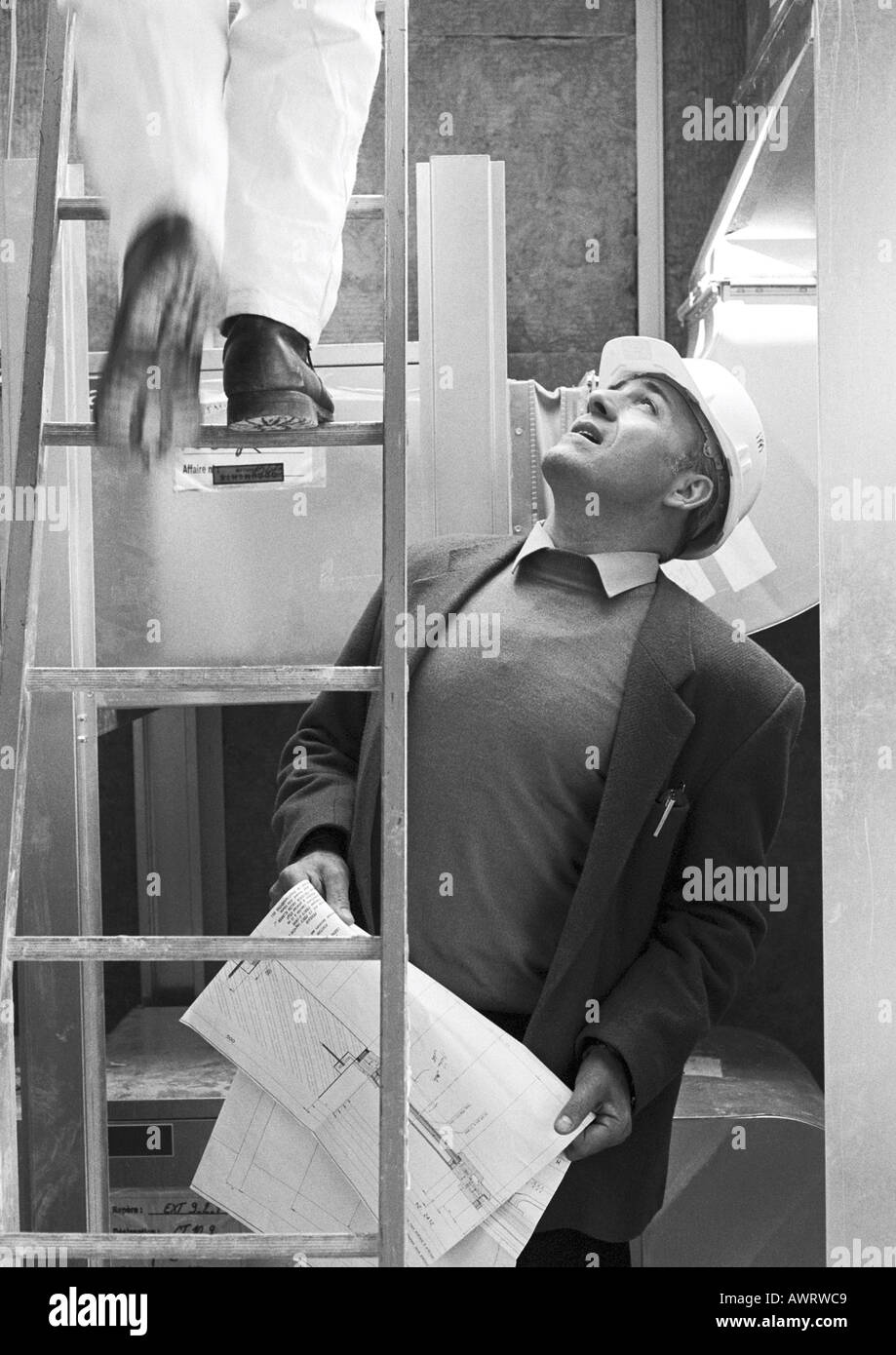 Man with hard hat looking at man sur l'escabeau, b&w Banque D'Images