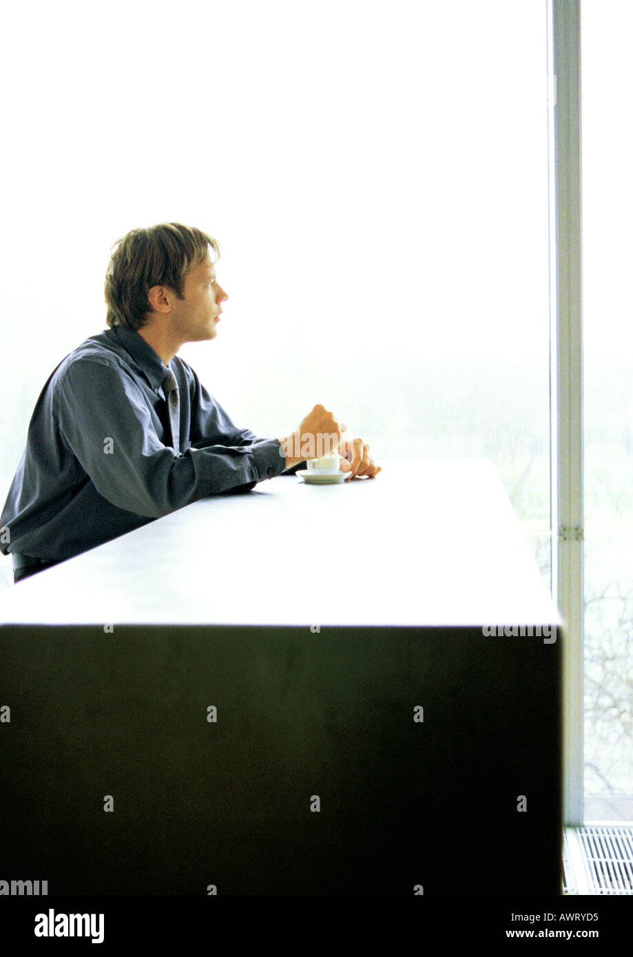 Businessman sitting at desk with coffee, à la fenêtre de Banque D'Images